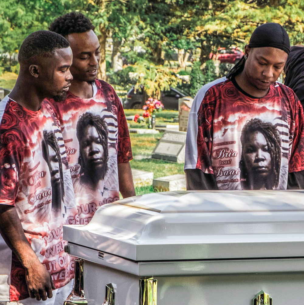 three men in memorial shirts around a coffin